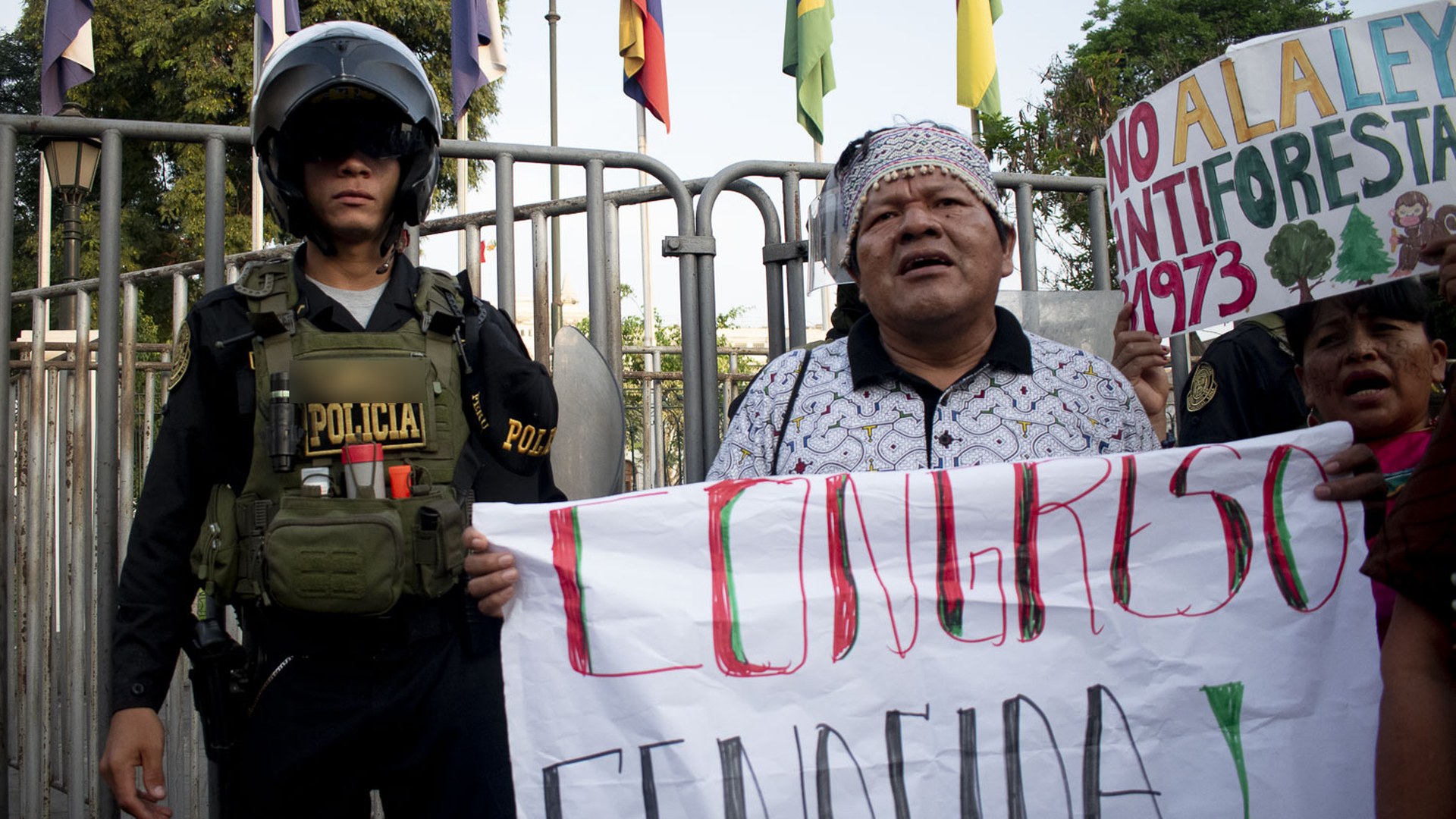 Ein Demonstrant mit gemustertem Stirnband hält ein Banner mit der Aufschrift „Congreso genocida“ neben einem Polizisten bei einem Marsch in Lima.